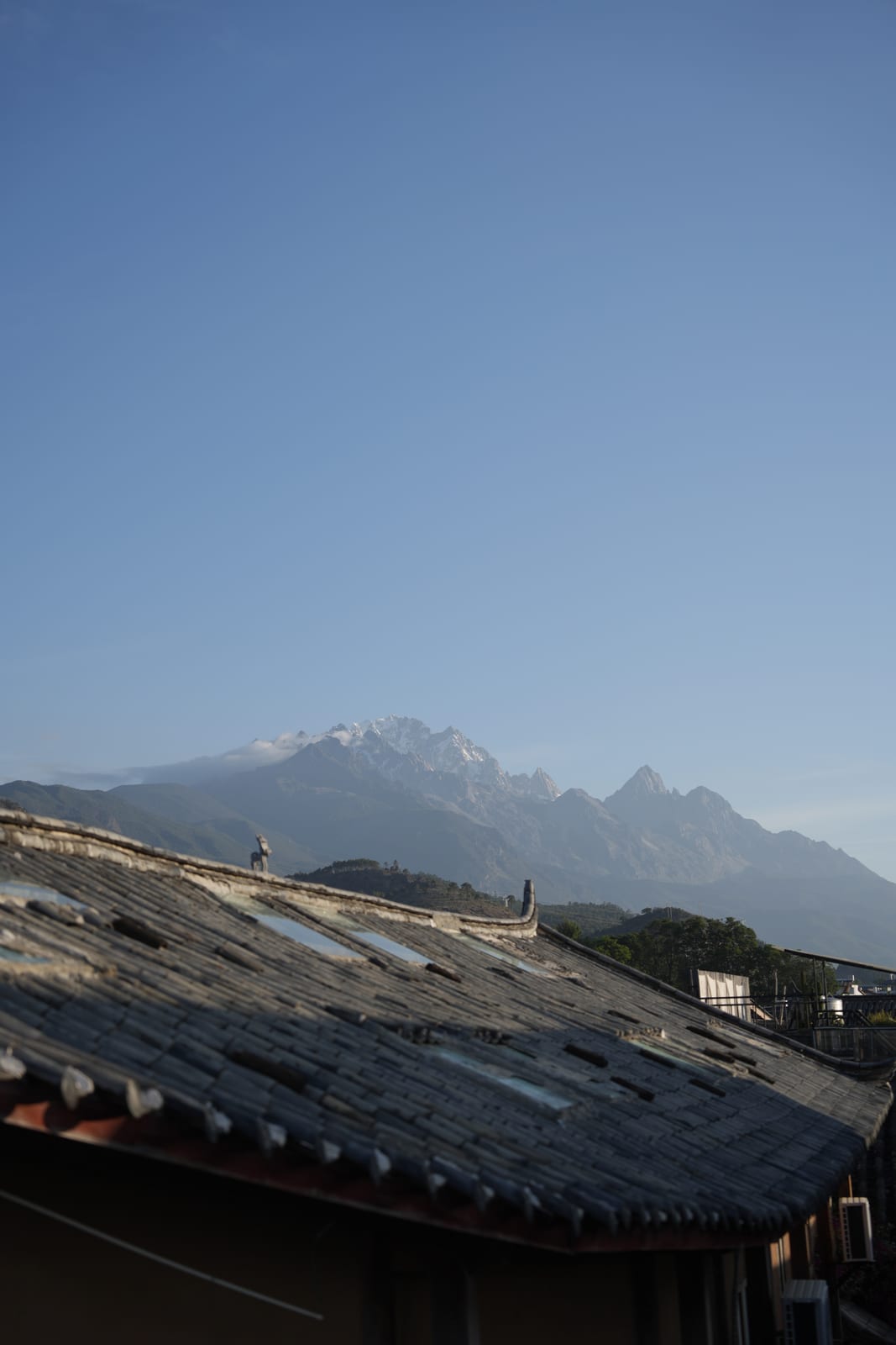 Naxi slate rooftops with Jade Dragon Snow Mountain rising behind in morning mist, Lijiang