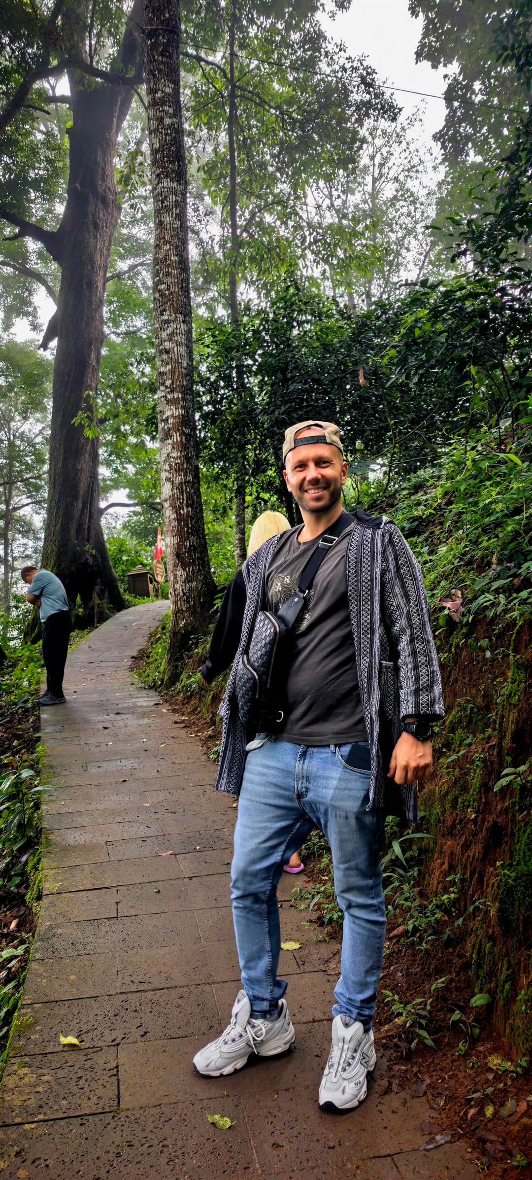 Mario on the stone walkway through Nannuo's ancient tea forest, mist hanging in the canopy