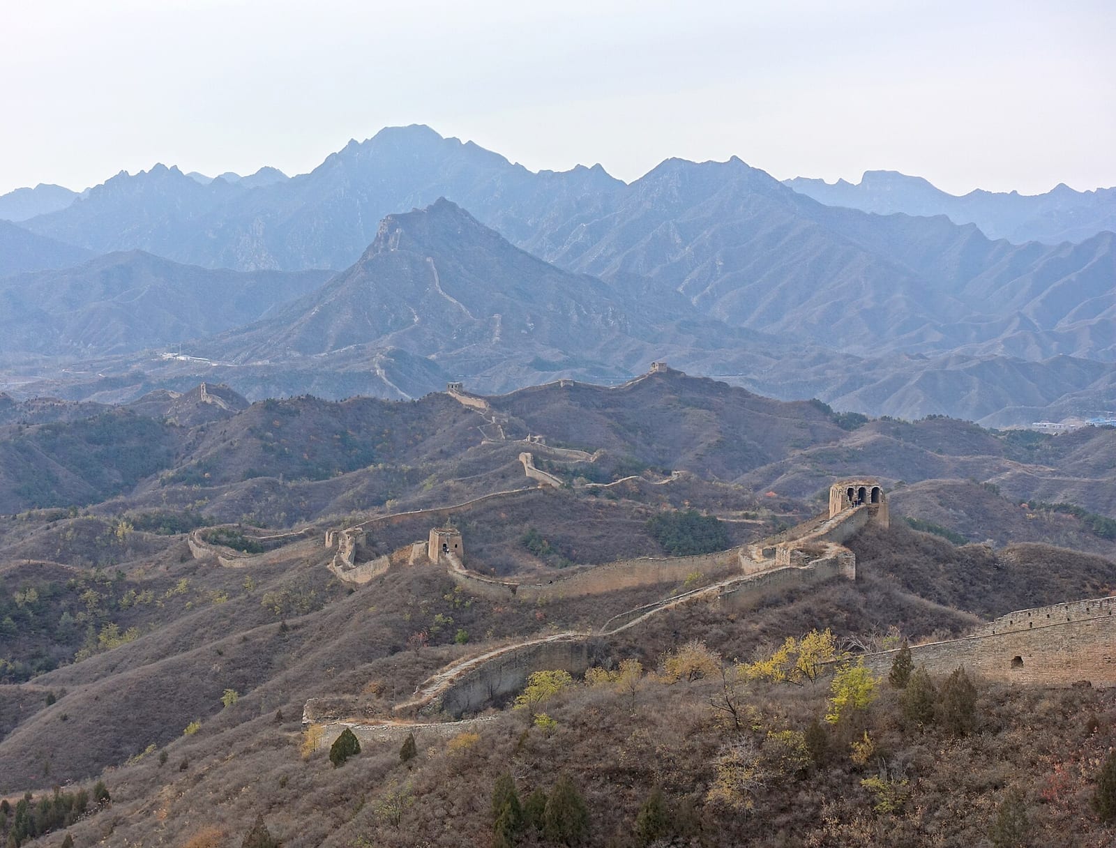 Unrestored Great Wall at Gubeikou winding over bare autumn ridges past ruined watchtowers, big mountains behind — day one of the wild-wall walk to Jinshanling