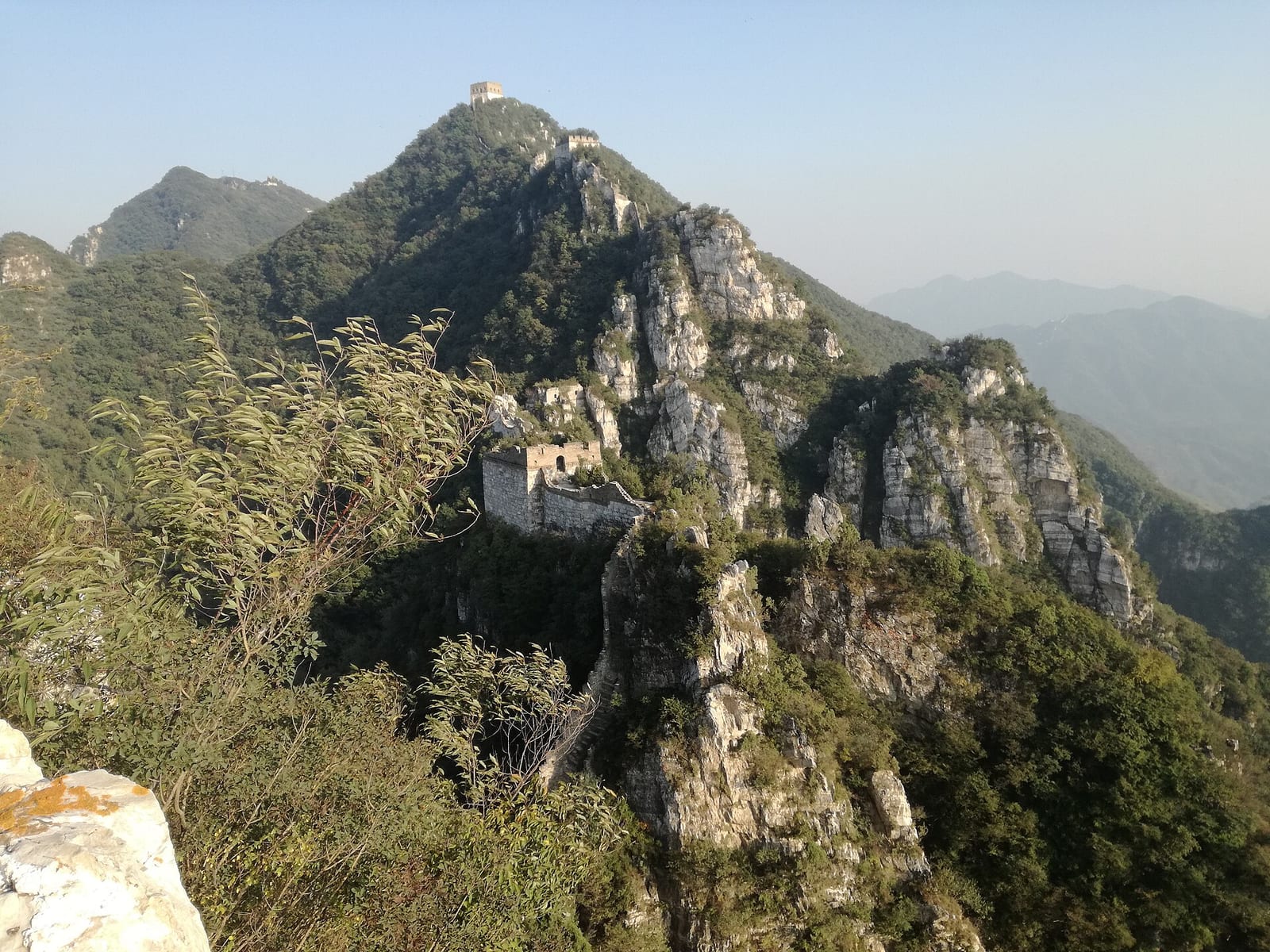 A ruined watchtower and crumbling wall clinging to white limestone crags at Jiankou, towers on the summit above — spectacular, and a genuinely risky climb