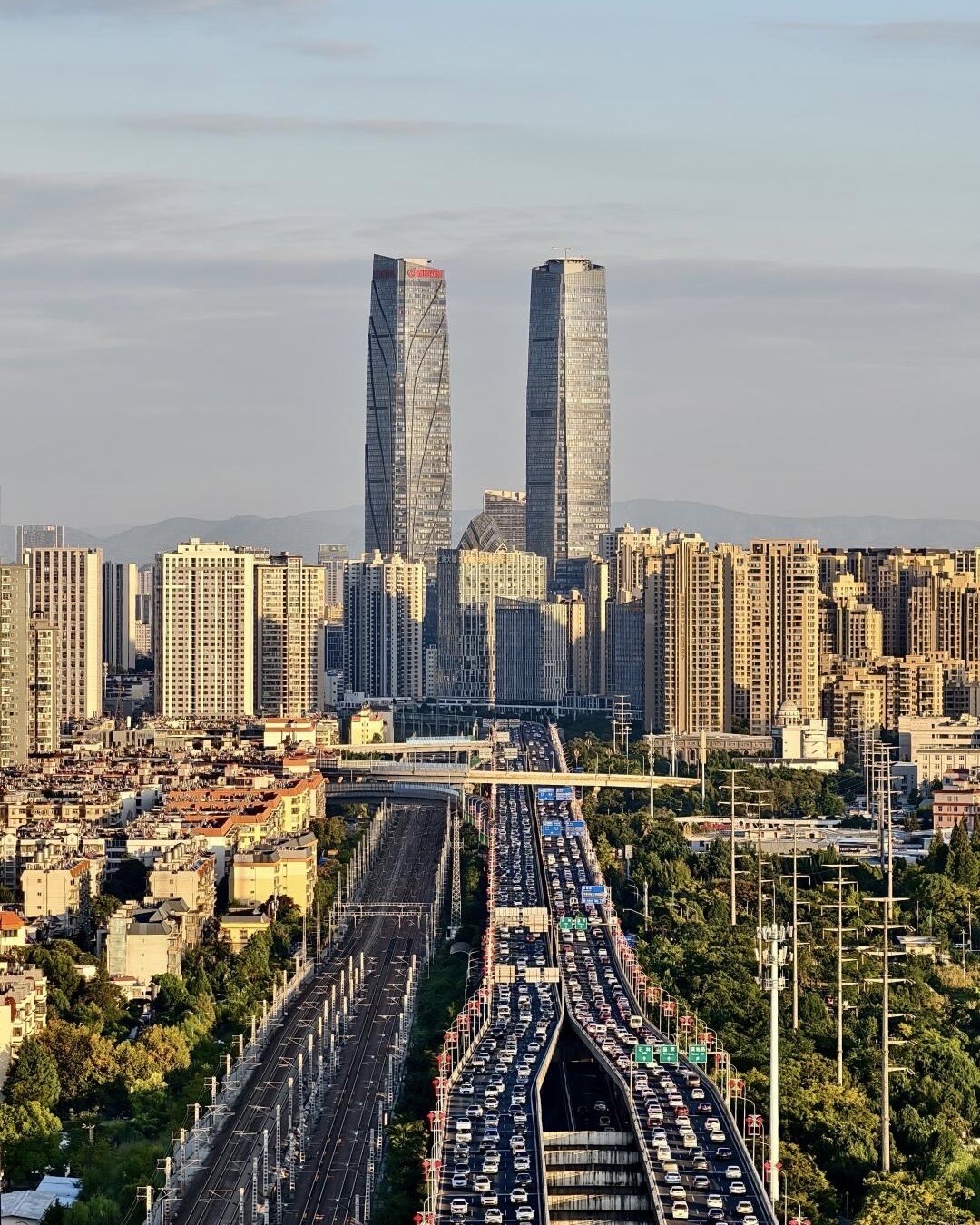Kunming twin-tower skyline above dense high-rises, with traffic-clogged elevated expressway and rail lines below