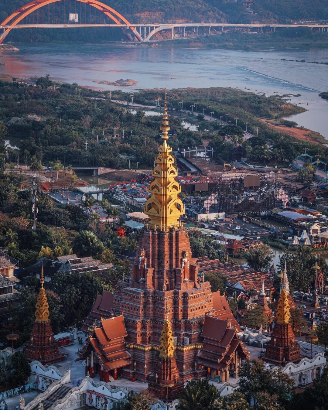 Aerial view of a golden-spired Dai temple beside the Mekong River and arched bridge, Xishuangbanna