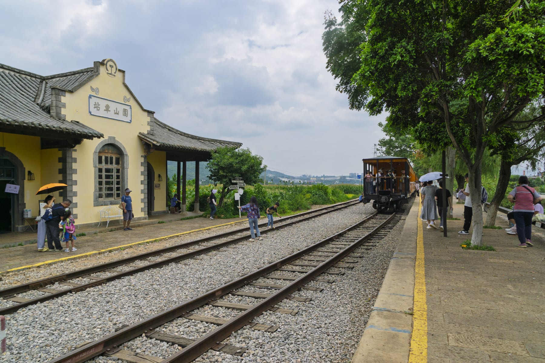 The Jianshui small train arriving at Tuanshan station, a yellow station building beside the metre-gauge track