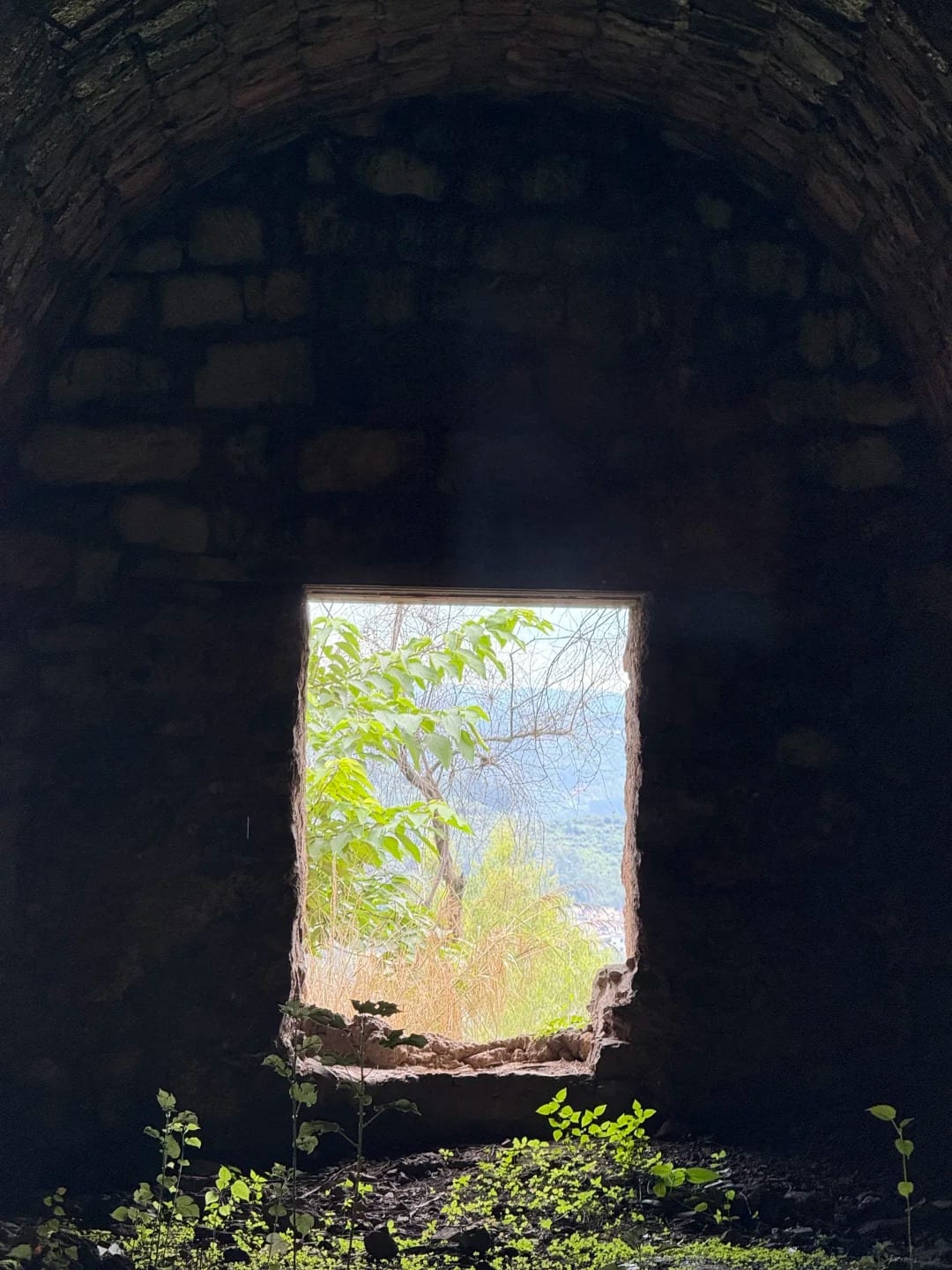 A window cut through the wall of a tunnel on the Yunnan–Vietnam Railway, framing the green hillside outside