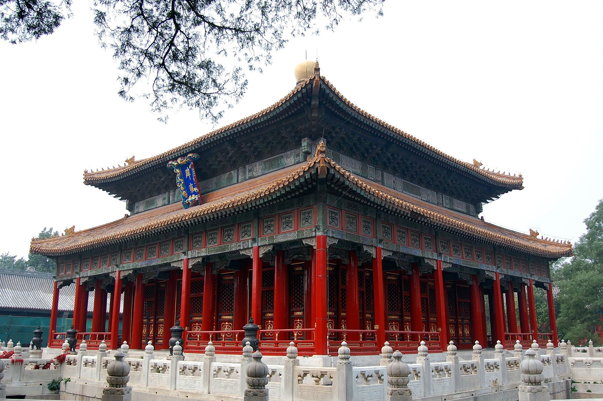 The upturned eaves and red colonnade of the main hall at the Confucius Temple (孔庙) under tree cover, Beijing