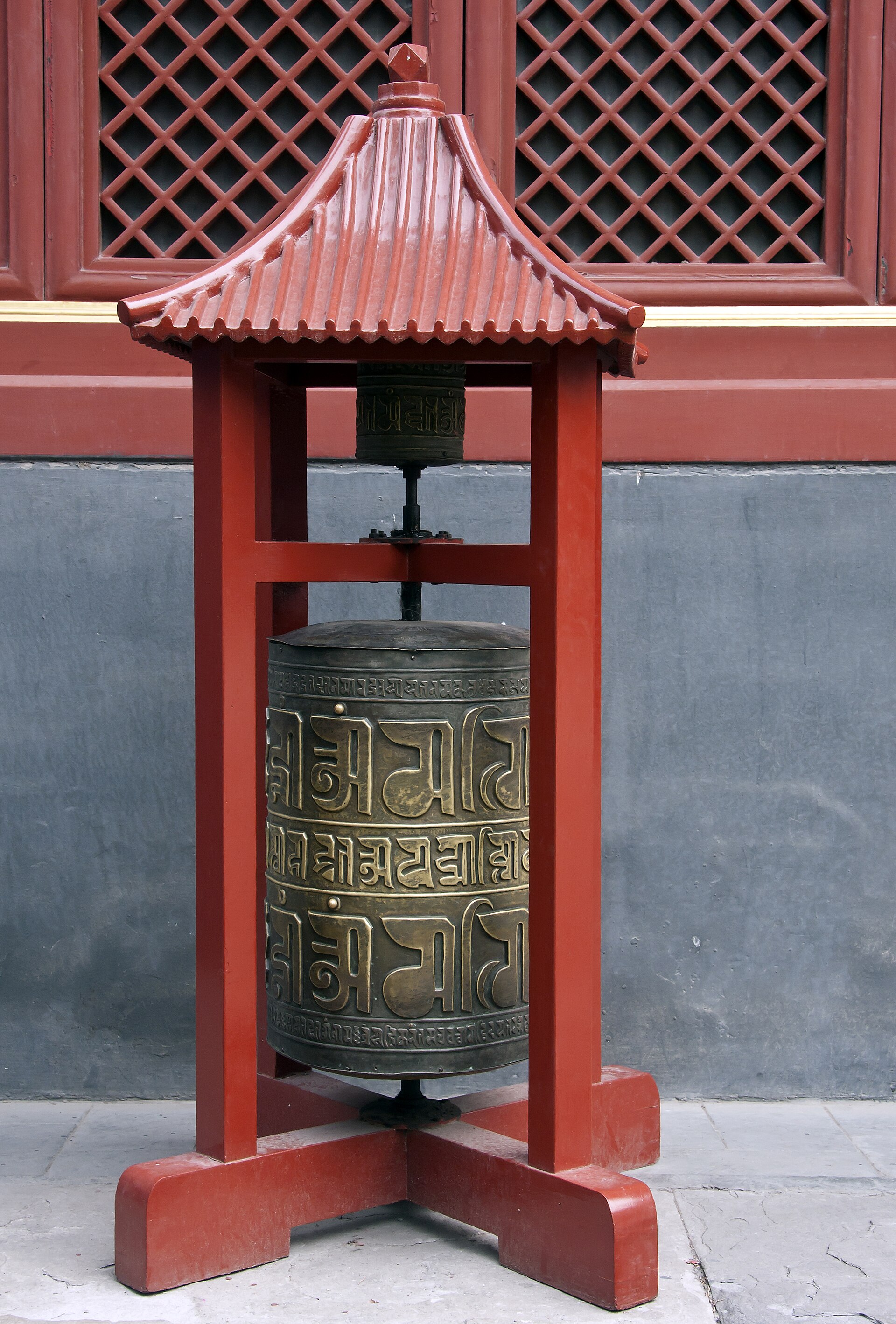 A bronze prayer wheel under a red pavilion roof against the lattice windows of the Yonghe Lama Temple (雍和宫), Beijing
