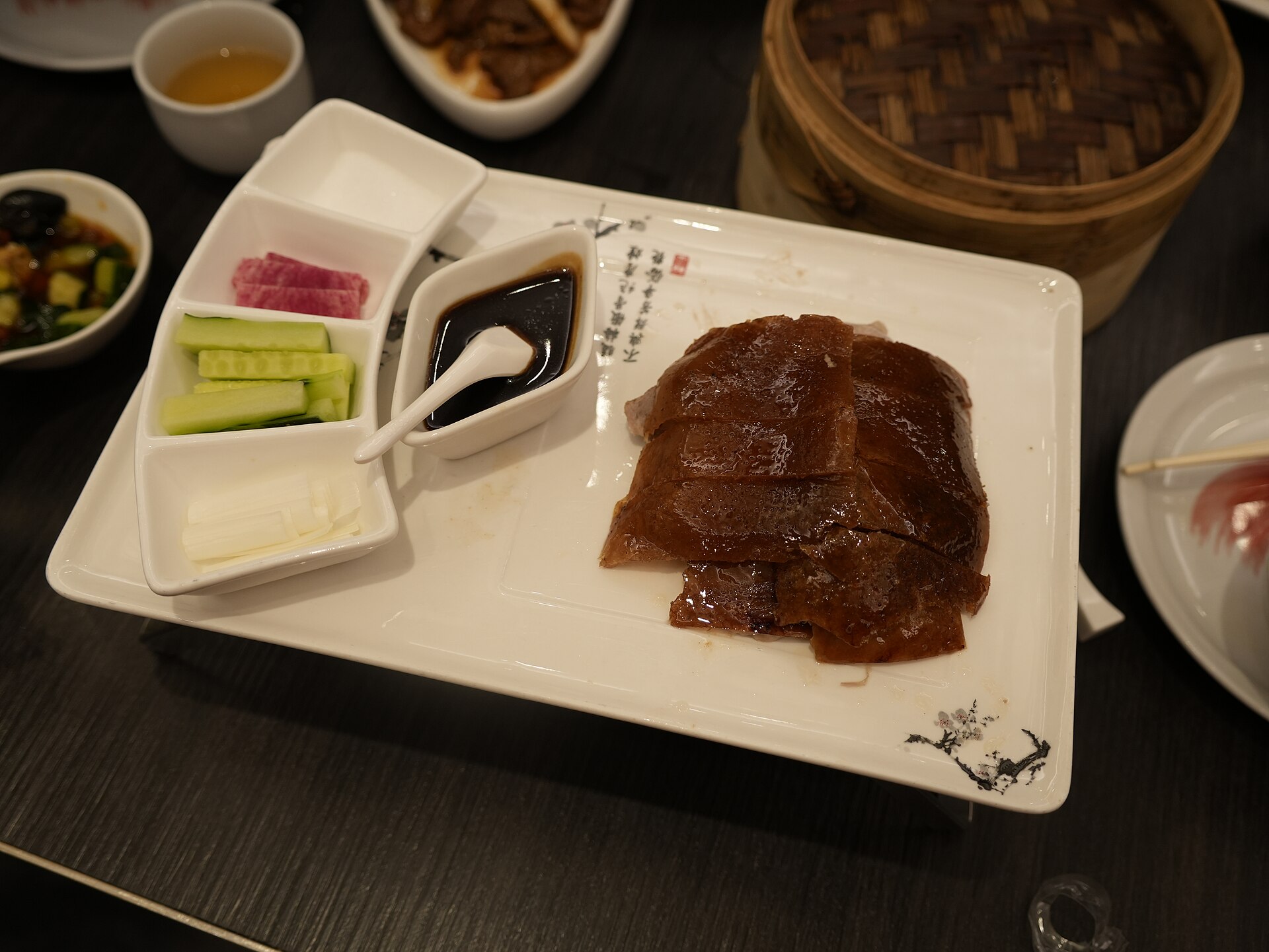 Lacquered Peking duck — mahogany skin and sliced meat plated with cucumber, scallion, sweet bean sauce and a steamer of thin pancakes, Beijing