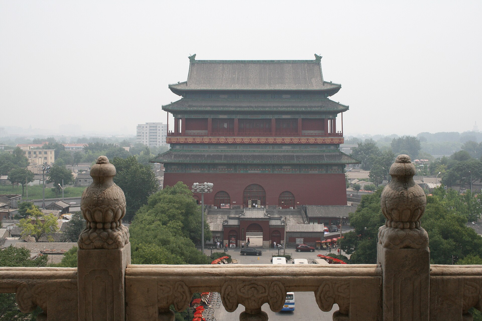 The Drum Tower (鼓楼) rising above the grey-tiled rooftops and summer-green trees of the old lanes, seen from the Bell Tower, Beijing