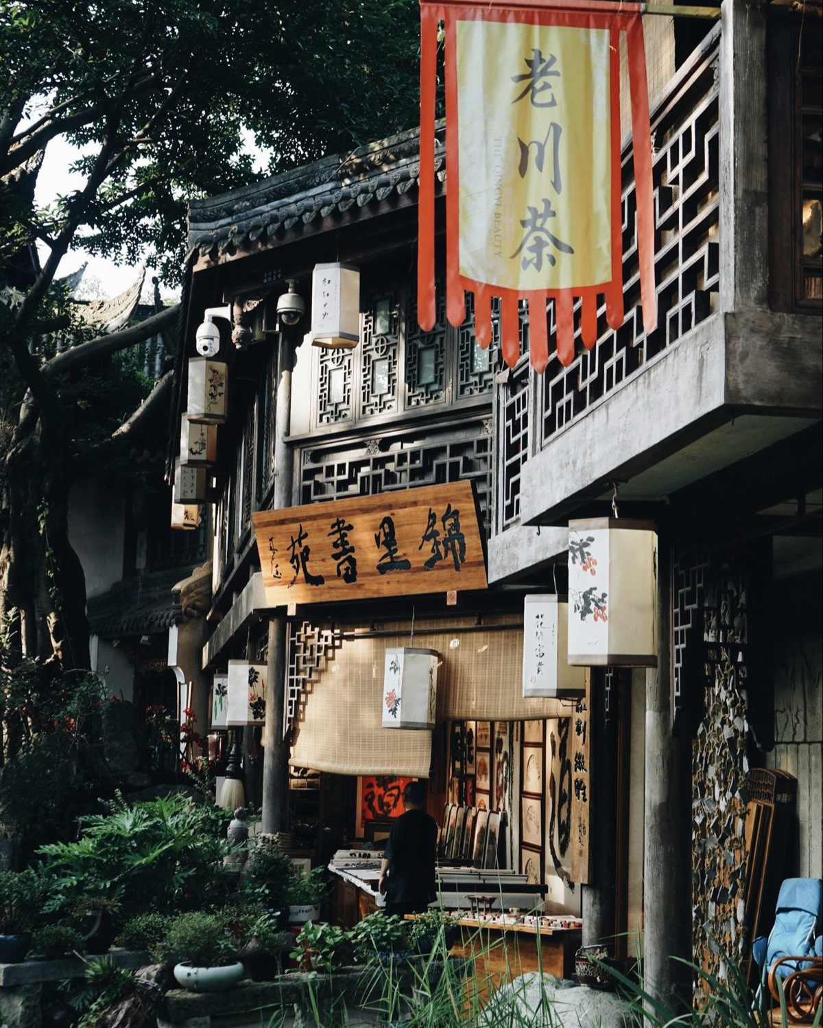 Old Chengdu teahouse street with a carved wooden shop sign, hanging paper lanterns and a red tea banner.