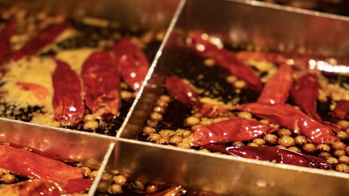Close-up of dried red chillies and peppercorns steeping in fragrant oil in metal trays, the base of Sichuan hotpot in Chengdu.