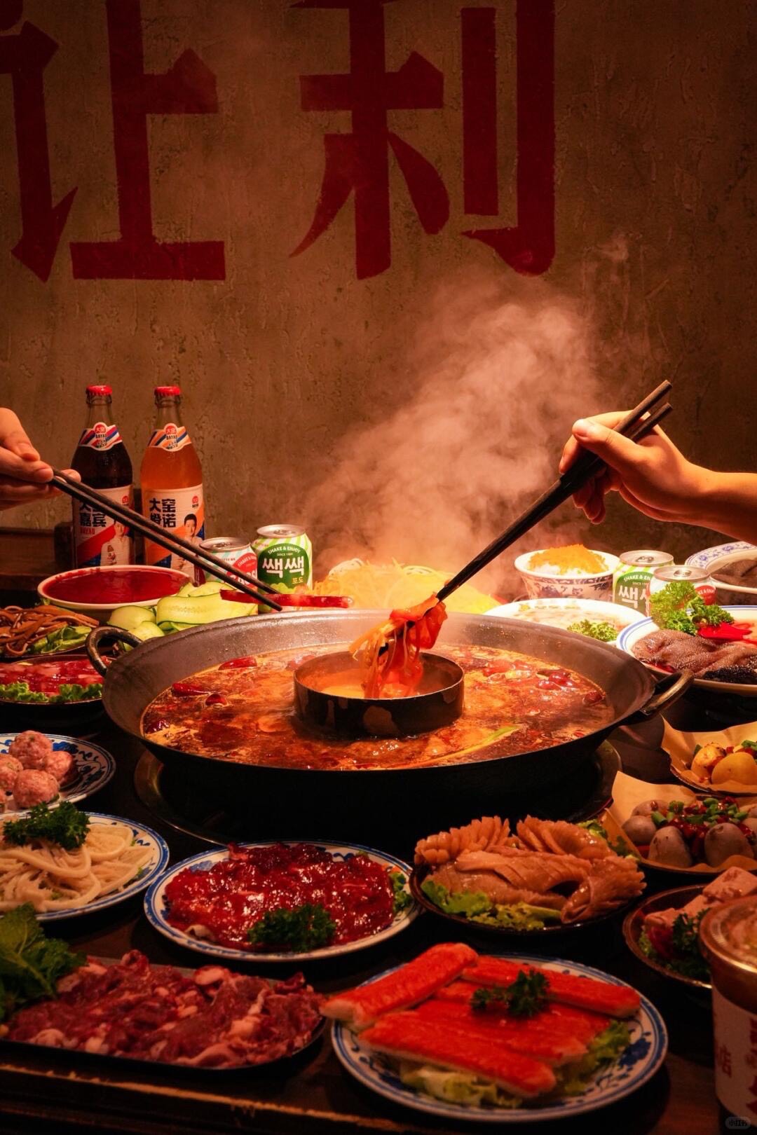 Steaming red Sichuan hotpot ringed by plates of sliced meats and vegetables as diners lift food with chopsticks in Chengdu.