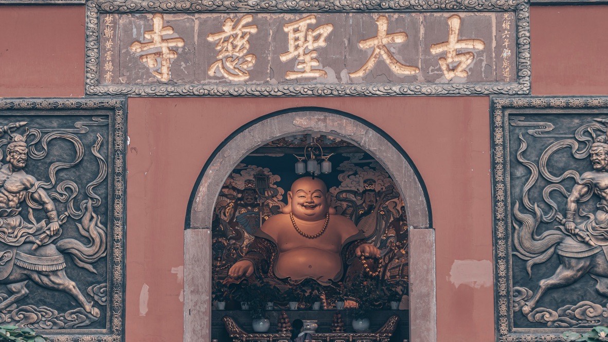 Chengdu temple gate with gilt Chinese characters, a smiling seated Buddha in the arch and carved guardian reliefs.