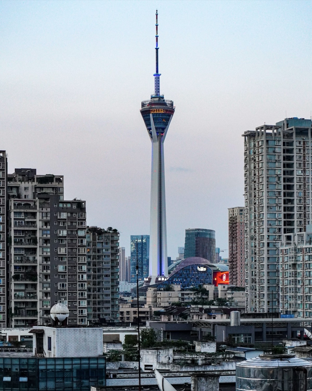 Chengdu's needle-topped observation tower rising above high-rise apartment blocks and city rooftops at dusk.