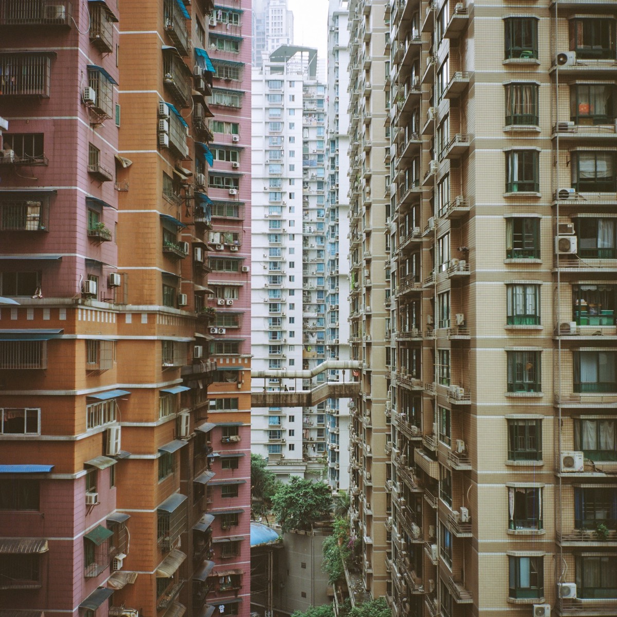 Densely packed colourful high-rise apartment blocks in Chongqing with a walkway bridging two towers over the valley below.