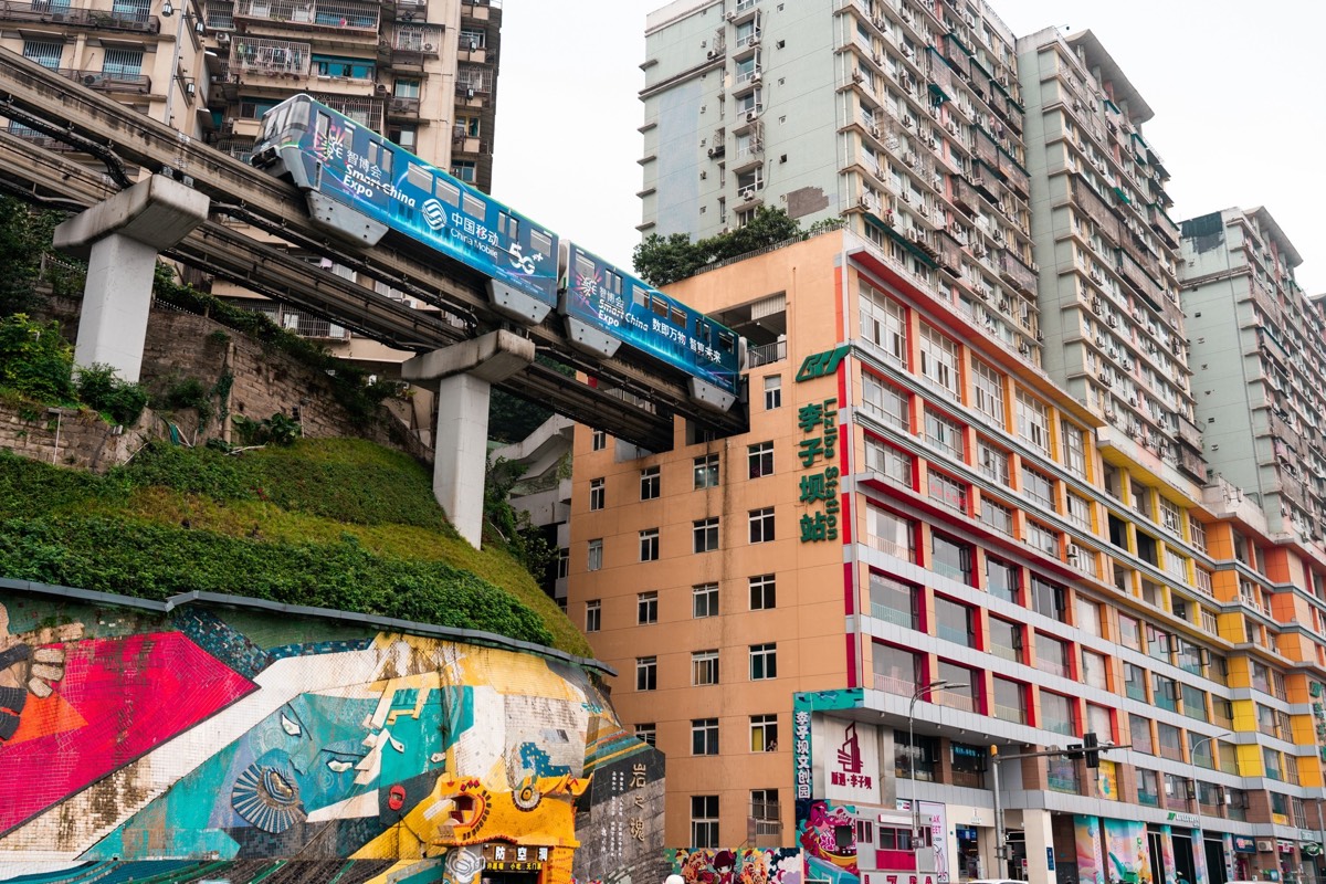 Chongqing monorail train passing through the mid-levels of a residential building at Liziba Station above a street mural.