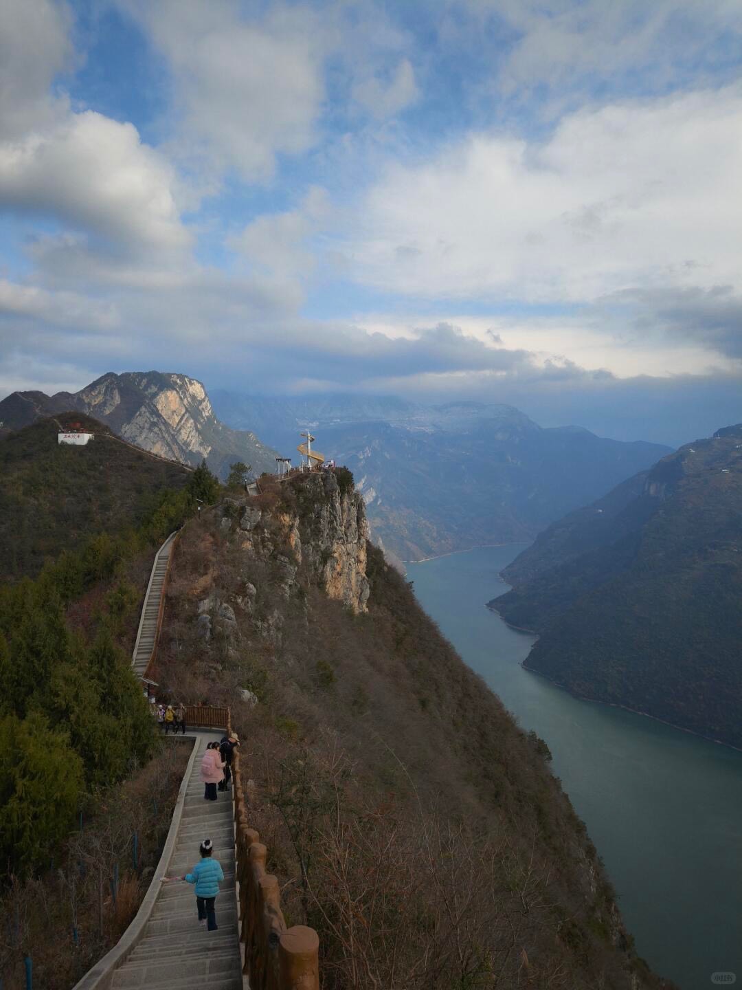 Visitors descending a clifftop stairway to a river-gorge viewpoint high above the winding green water below Chongqing.