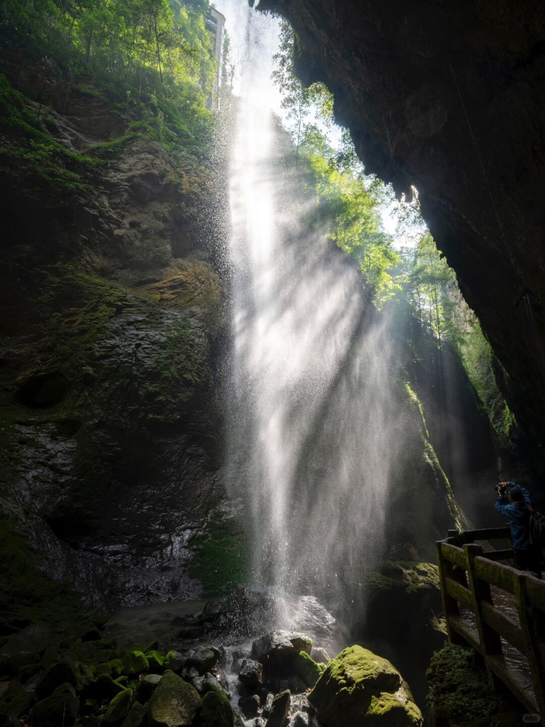 Waterfall plunging into a cavern as sunlight streams past a viewing platform in Chongqing's Wulong karst.