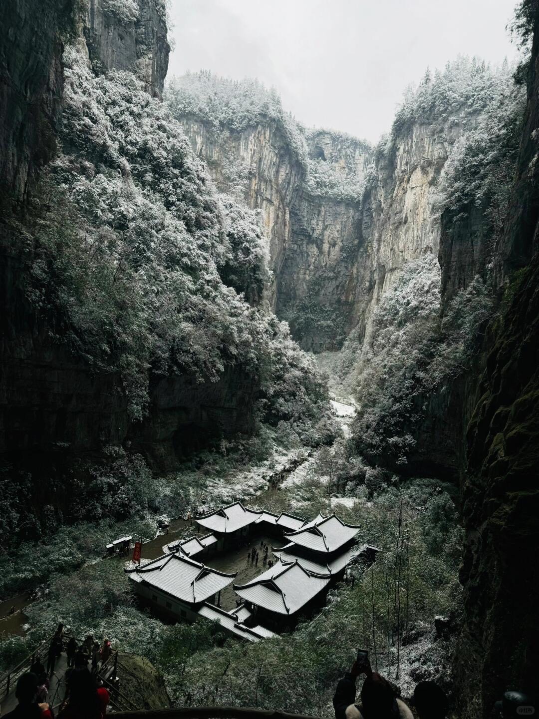 Snow-dusted karst cliffs towering over a tiled temple courtyard in Chongqing's Wulong natural bridge canyon.