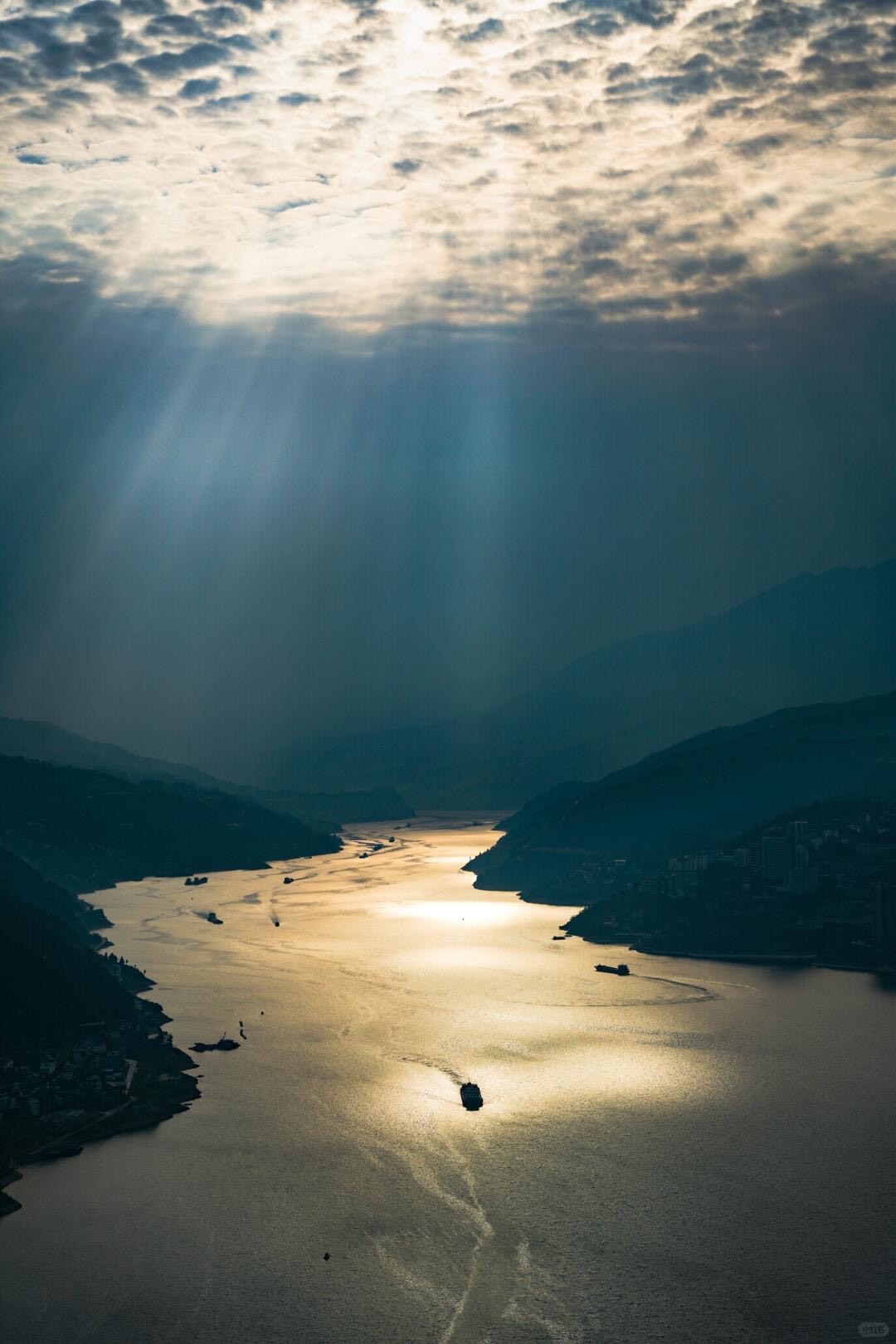 Sunbeams break through clouds over the Yangtze gorge as cruise ships trail wakes on the golden-lit river near Chongqing.