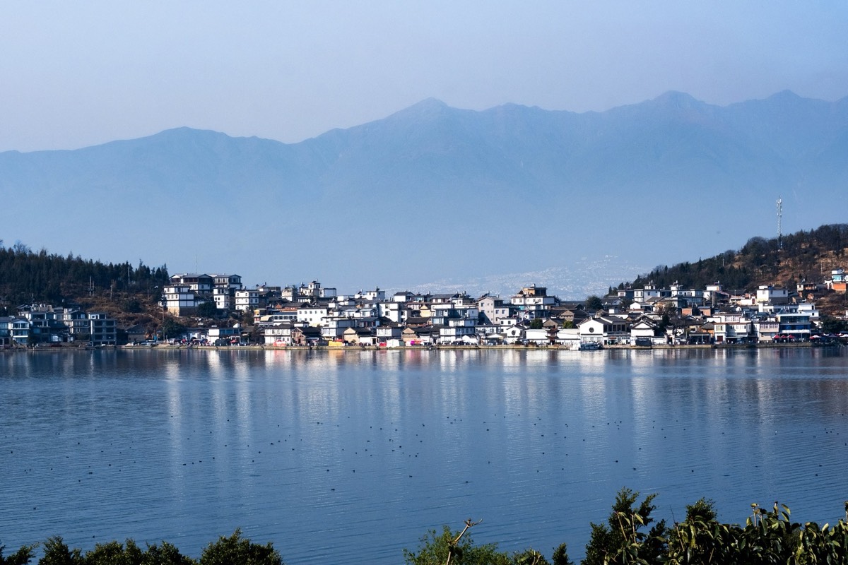 Erhai Lake mirroring the snow-capped Cangshan ridge behind a whitewashed Bai village, Dali — Classic China & Yunnan tour