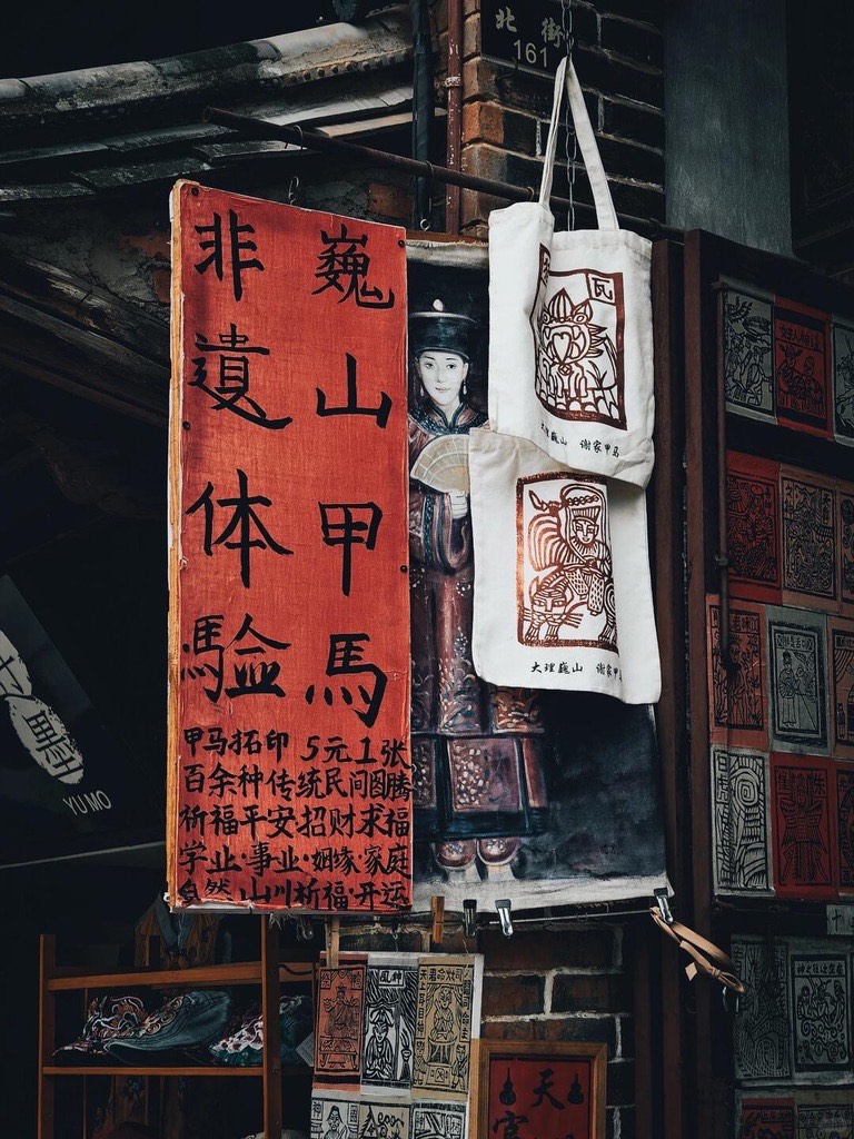 Weishan craft stall selling jiama folk woodblock prints and tote bags beside a red hand-lettered sign.