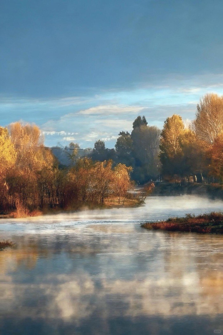 Mist rising off a still river lined with golden autumn trees under a blue sky near Shaxi.