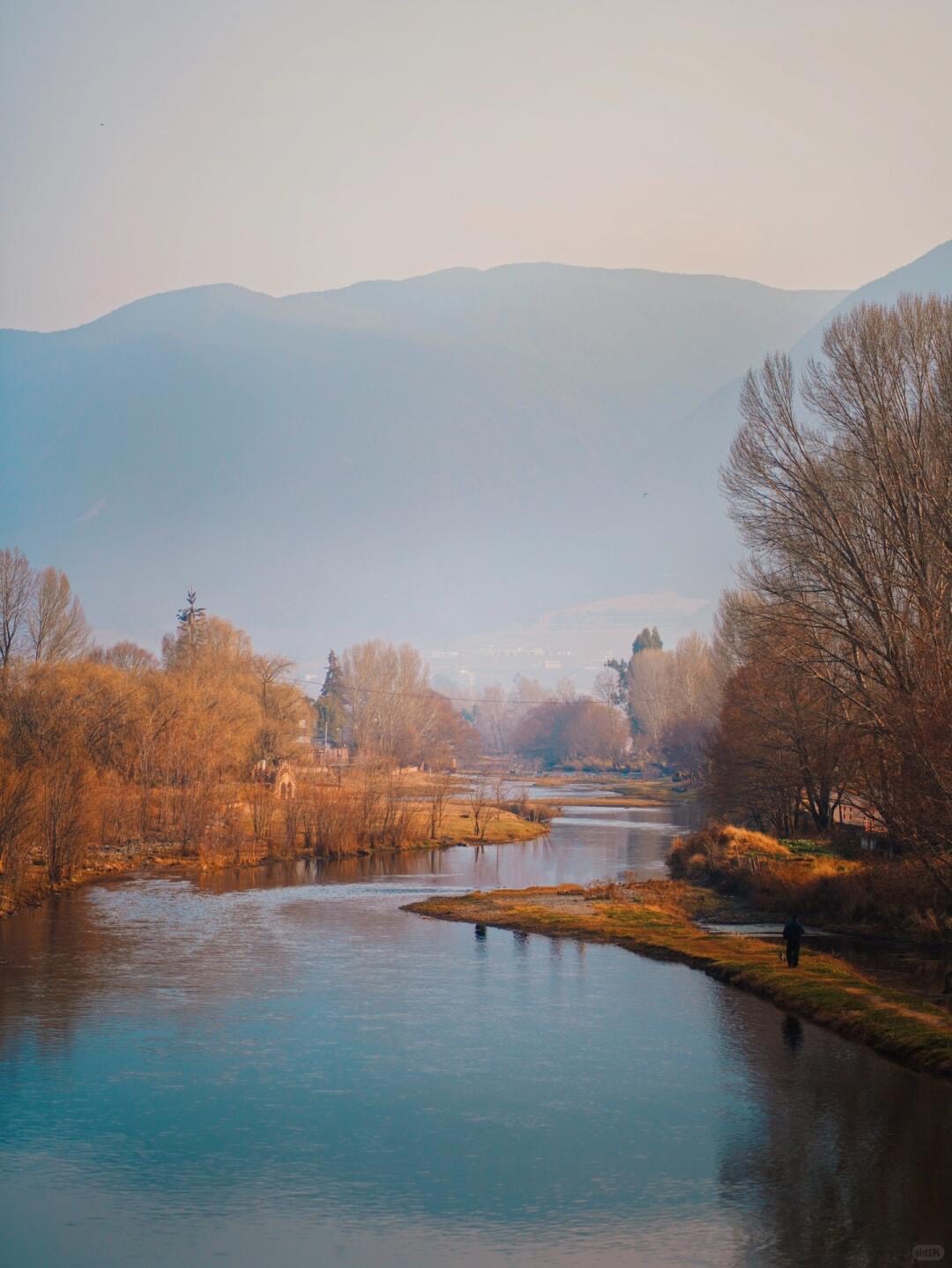 A calm river bends past bare golden trees toward hazy mountains at dusk near Shaxi on the tea horse road.