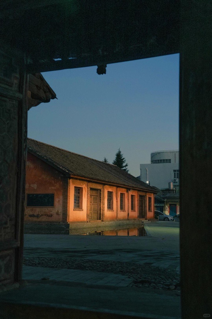 Warm-lit adobe building framed by a dark timber gateway at dusk in Weishan Ancient Town.