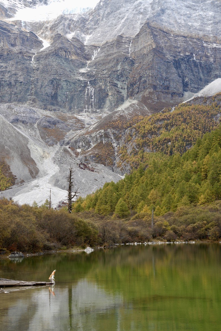 Turquoise-green alpine lake reflecting autumn larches and steep cliffs on the Yading short kora.