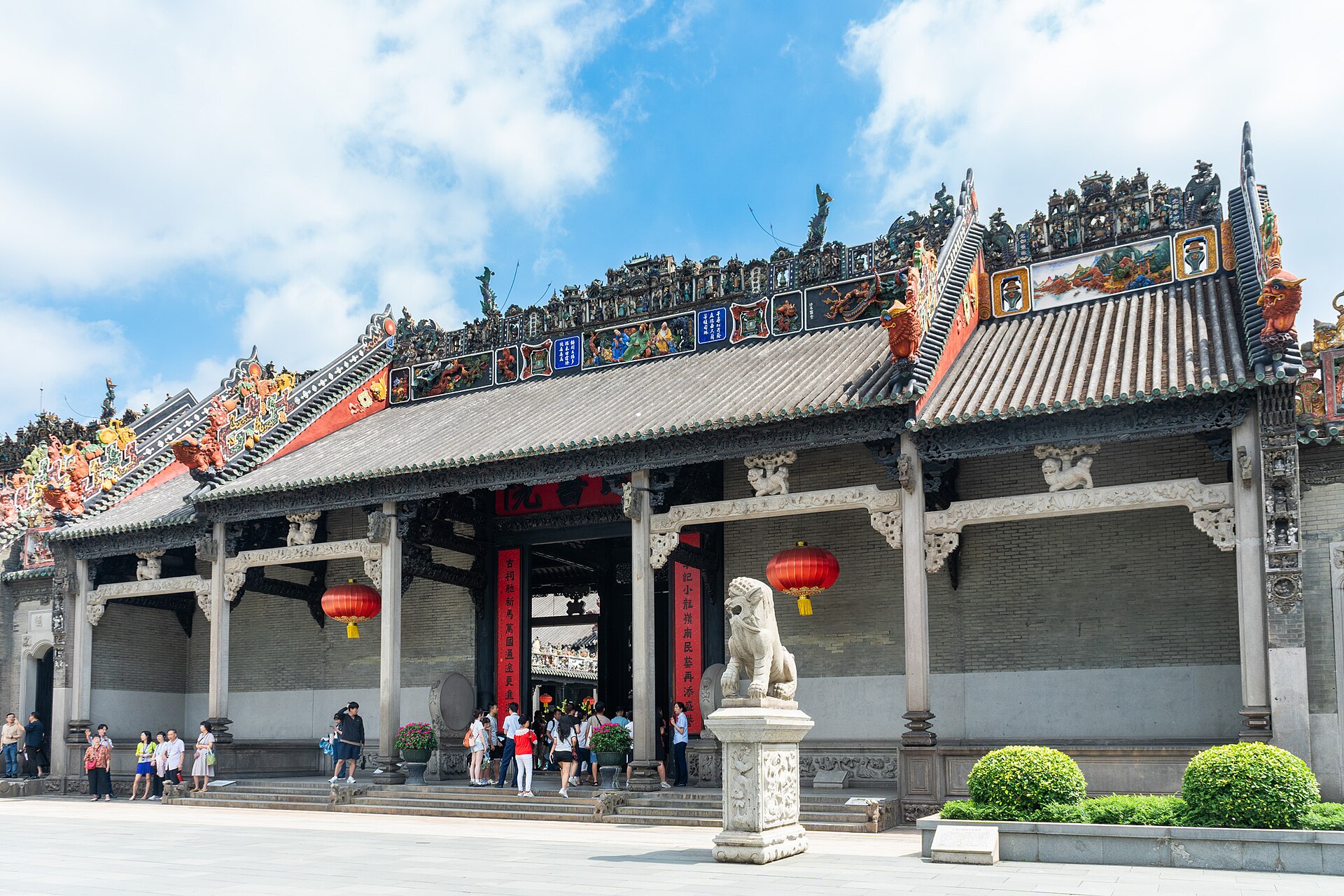 The Chen Clan Ancestral Hall (陈家祠) with a granite guardian lion and ornate carved roof ridges against a blue sky, Guangzhou