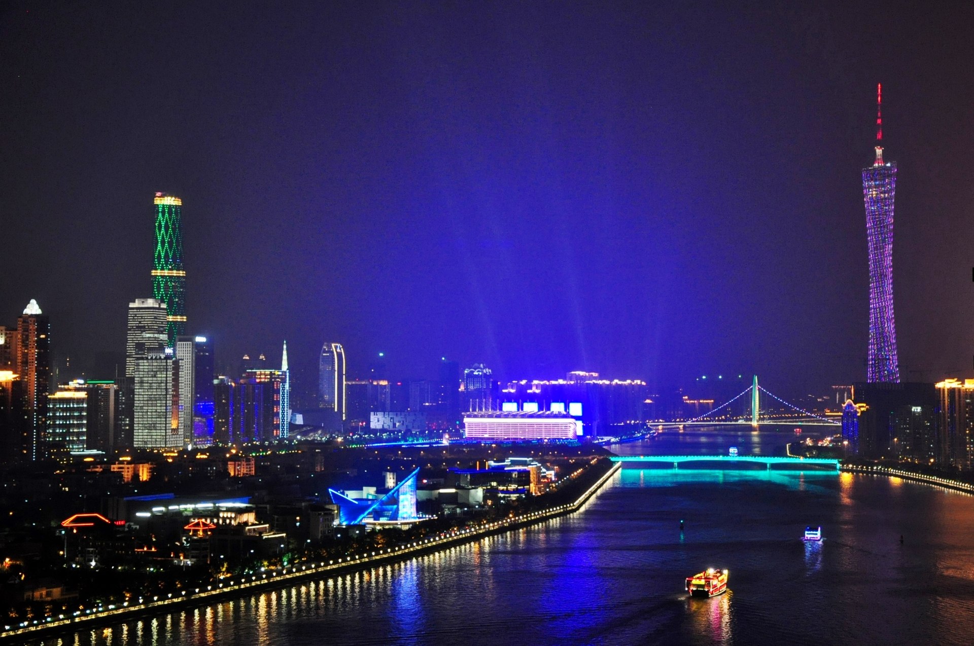 The Canton Tower (广州塔) glows beside the lit Zhujiang New Town skyline as light-show beams sweep above the Pearl River at night, Guangzhou