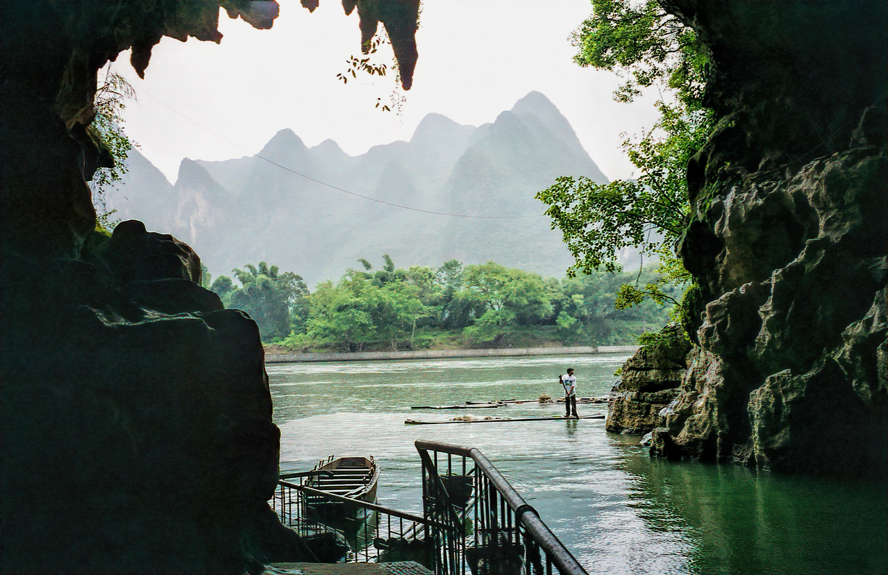 The Li River and misty karst peaks framed through the mouth of Crown Cave (冠岩), a boatman poling a raft, Guilin