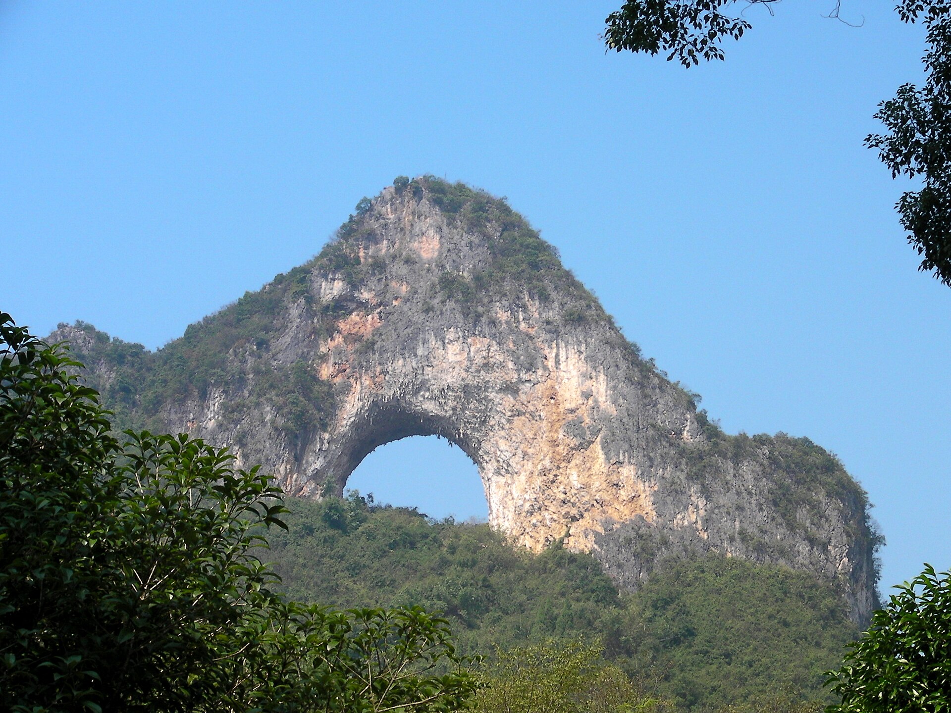 The natural arch of Moon Hill (月亮山) cutting through a karst ridge above green forest, Yangshuo, Guilin