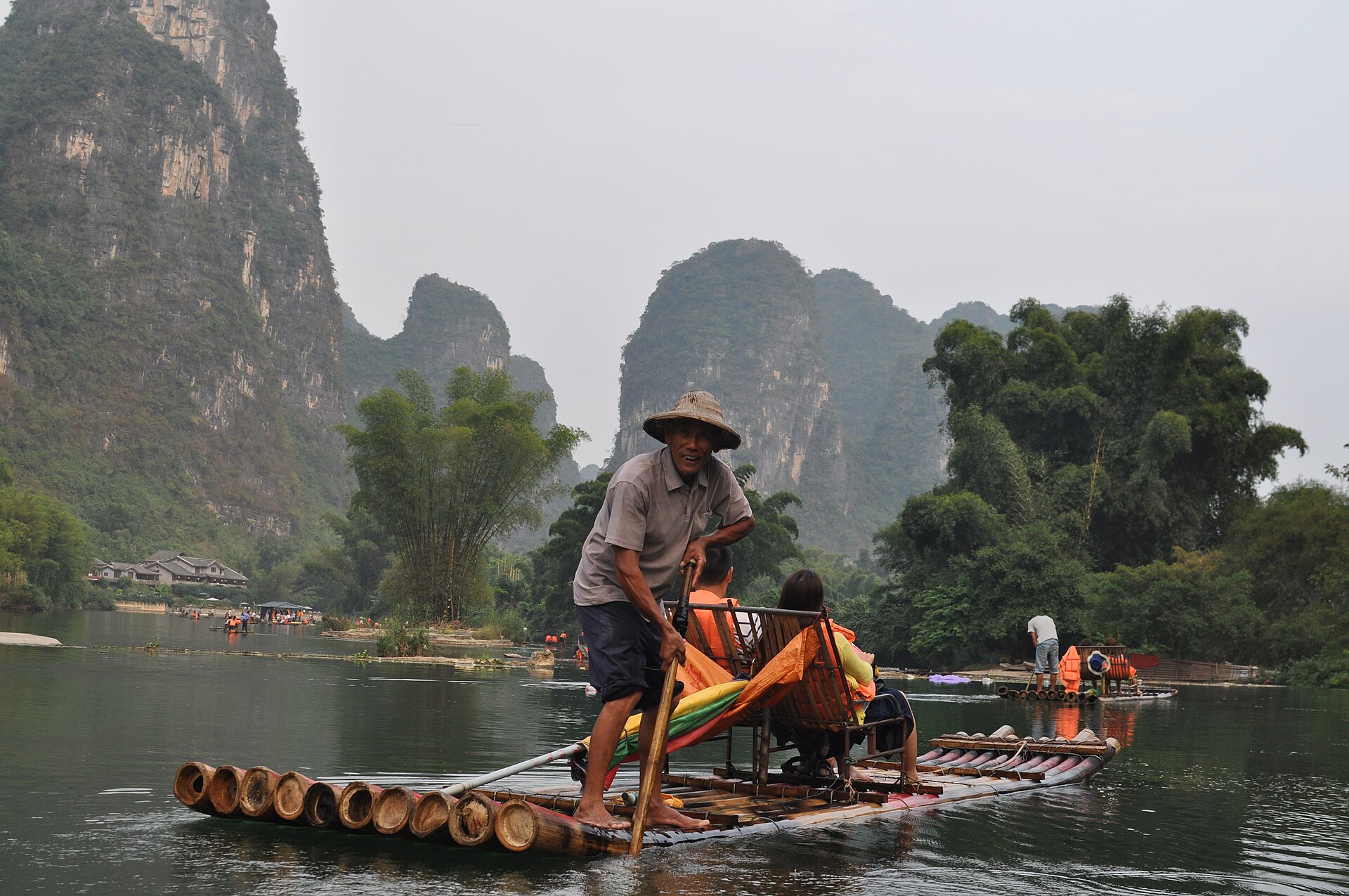 A boatman poling a bamboo raft down the Yulong River (遇龙河) beneath towering green karst peaks, Yangshuo, Guilin