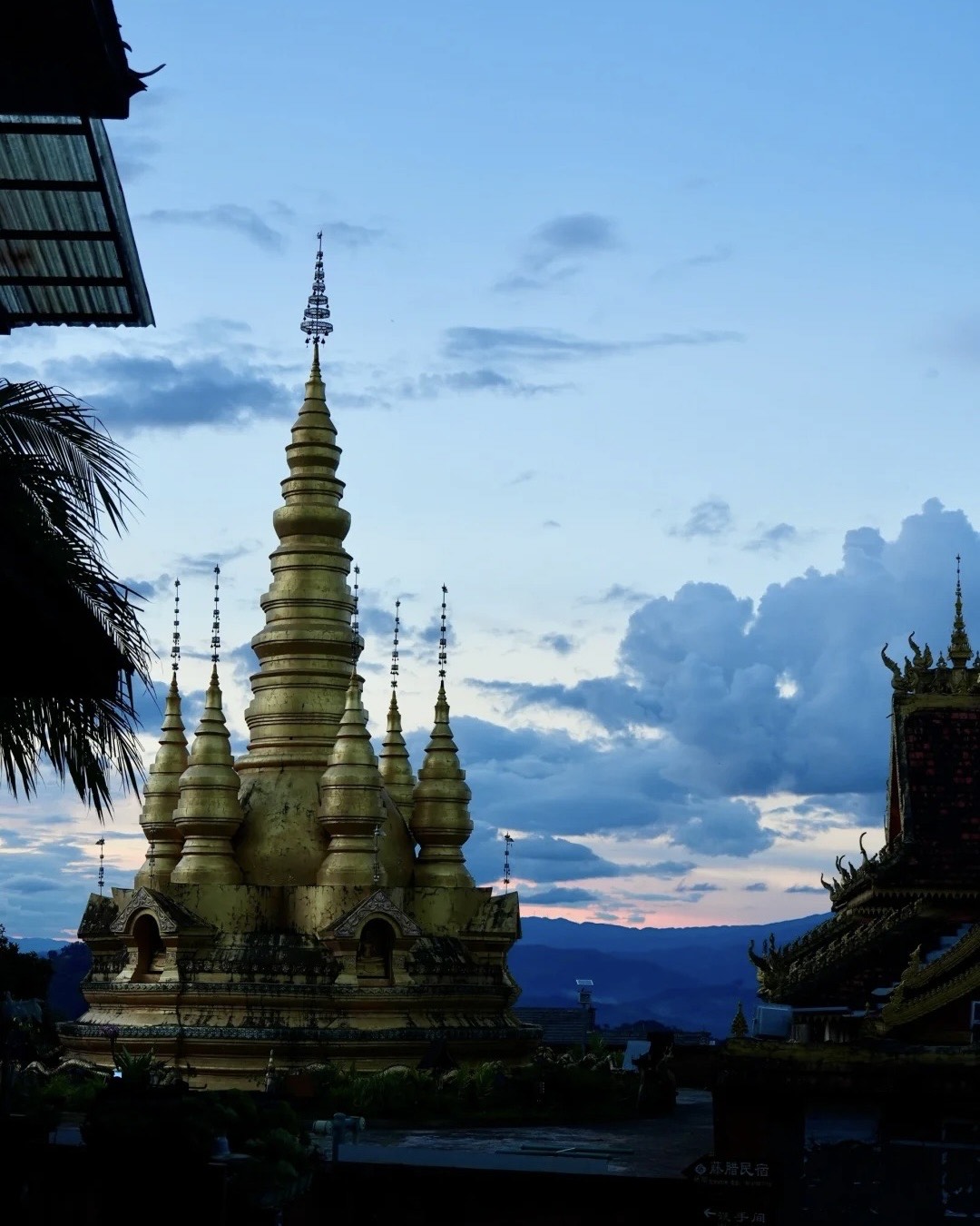 Golden multi-spired Buddhist stupa on Jingmai Mountain silhouetted against a blue dusk sky with distant hills