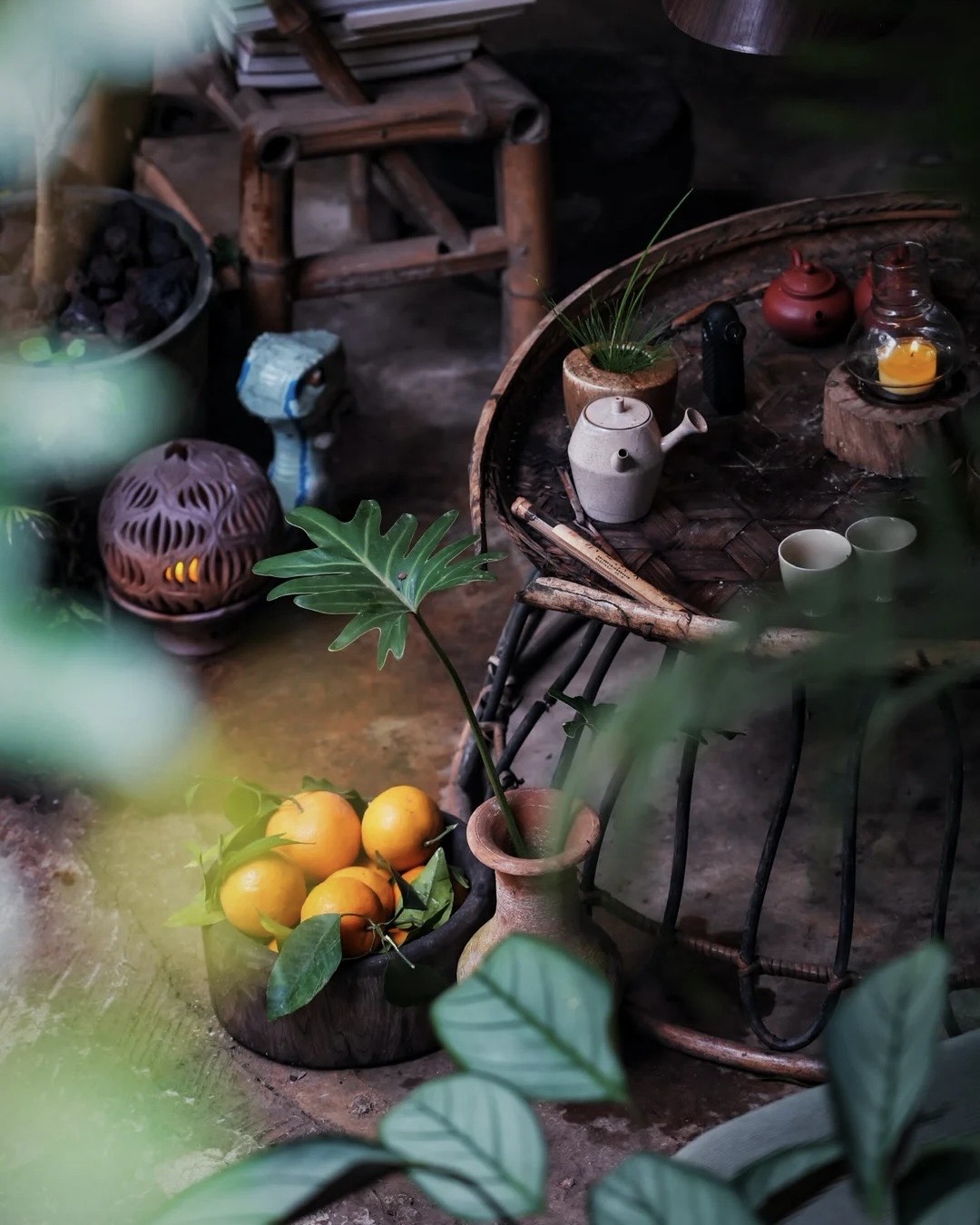 Rustic bamboo tea table with clay teapots, cups, a bowl of oranges and candlelight in a dim Jingmai forest hut.