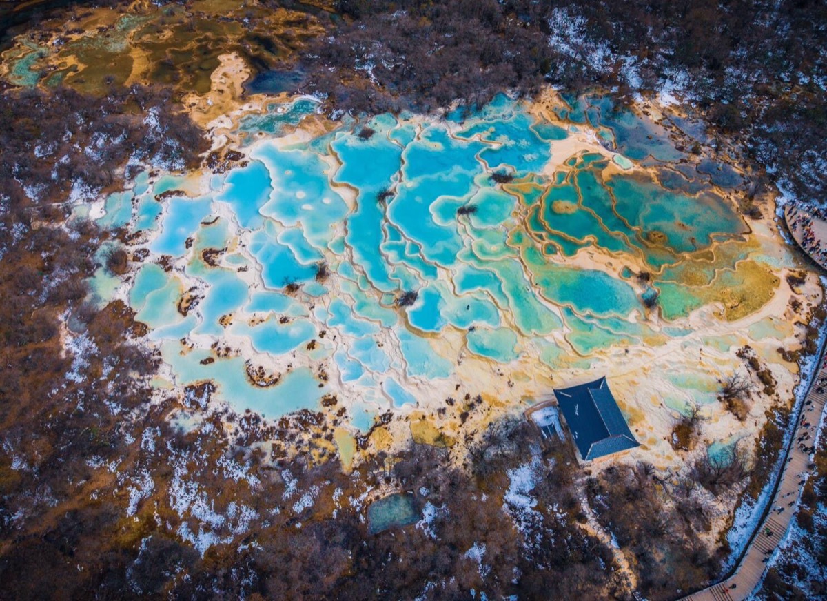 Aerial of Huanglong's Five Color Pool showing the temple pavilion and visitor boardwalk at the valley head