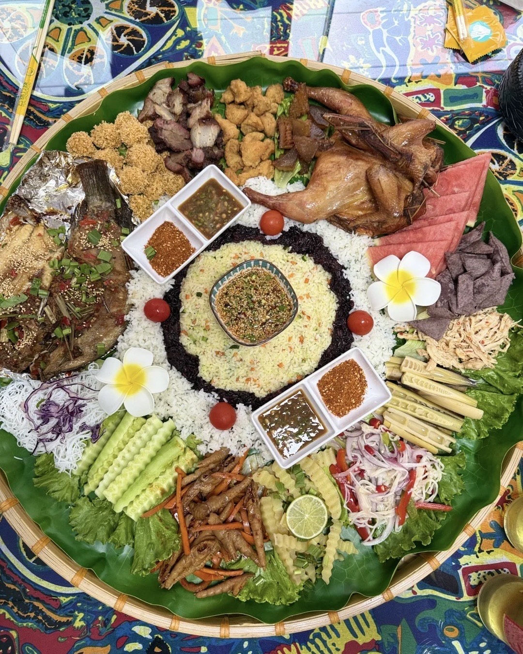 A large woven tray banquet of grilled meats, fish, rice and dipping sauces served on banana leaf in Kunming.