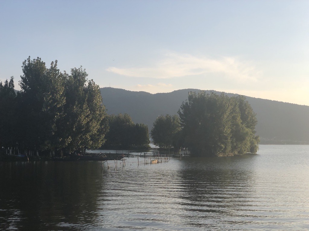 Tree-covered islets on the calm waters of Dianchi Lake below West Mountain in soft morning light near Kunming.