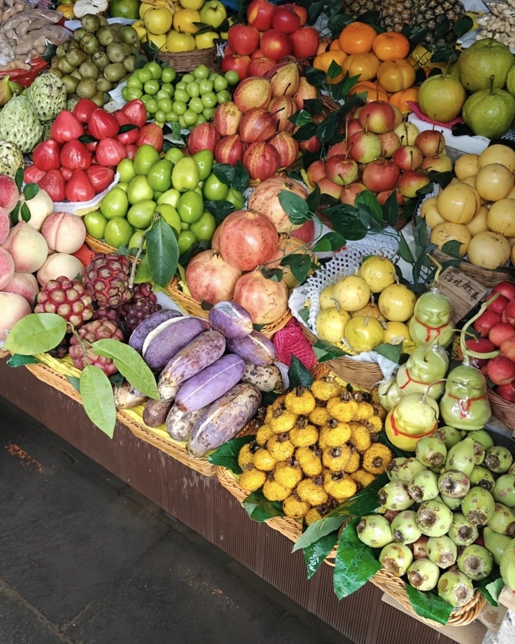 Colourful baskets of fresh fruit including rose apples, pomegranates and pears at a Kunming food market stall.