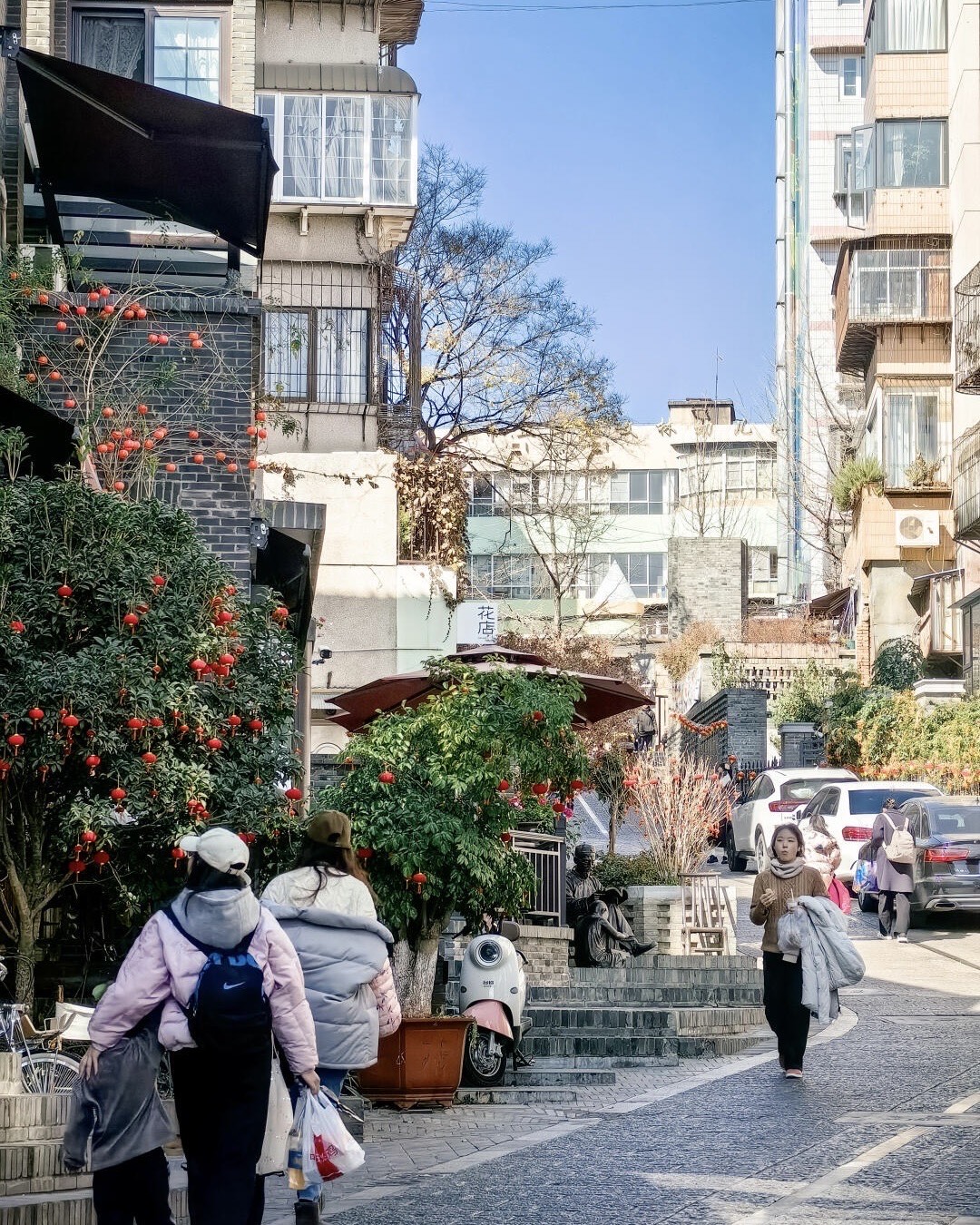 Sunny Kunming lane lined with old-brick buildings, a persimmon-laden tree and pedestrians in winter coats