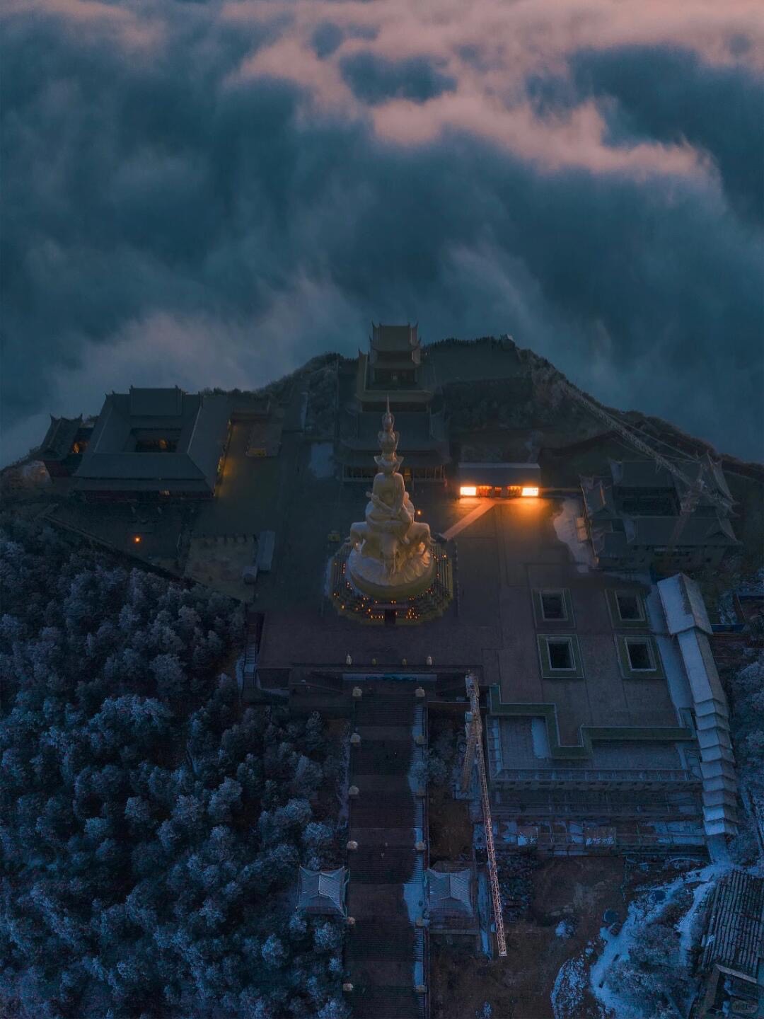 Aerial view of the golden summit statue and temples on frosted Mount Emei above a sea of clouds at dusk.