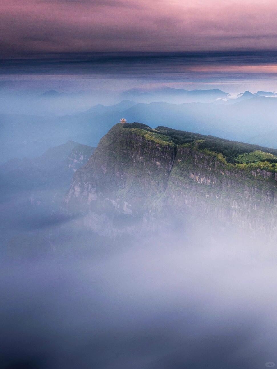 Cliff-top pavilion on Mount Emei's Golden Summit rising above a pink-tinged sea of clouds at dusk.