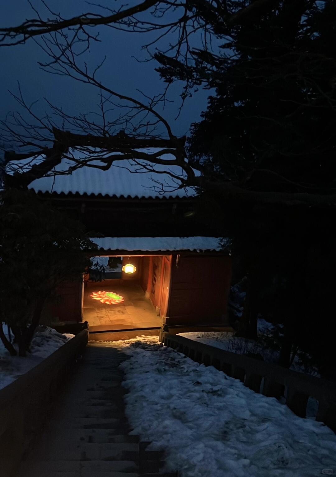 Snow-dusted temple gateway on Mount Emei glowing with a warm lantern and lotus light at dusk.