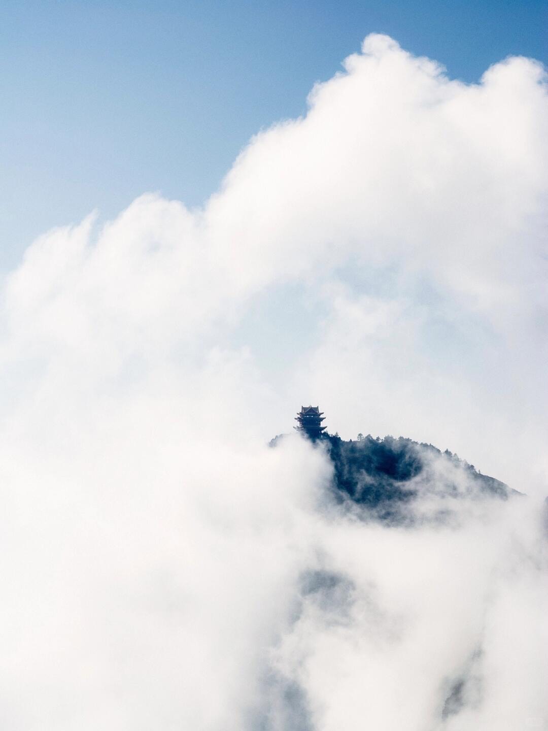 Distant summit pavilion on Mount Emei emerging from billowing white clouds under a clear blue sky.