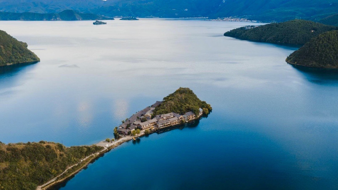 Aerial view of a small island village joined by a causeway on the calm blue waters of Lugu Lake.