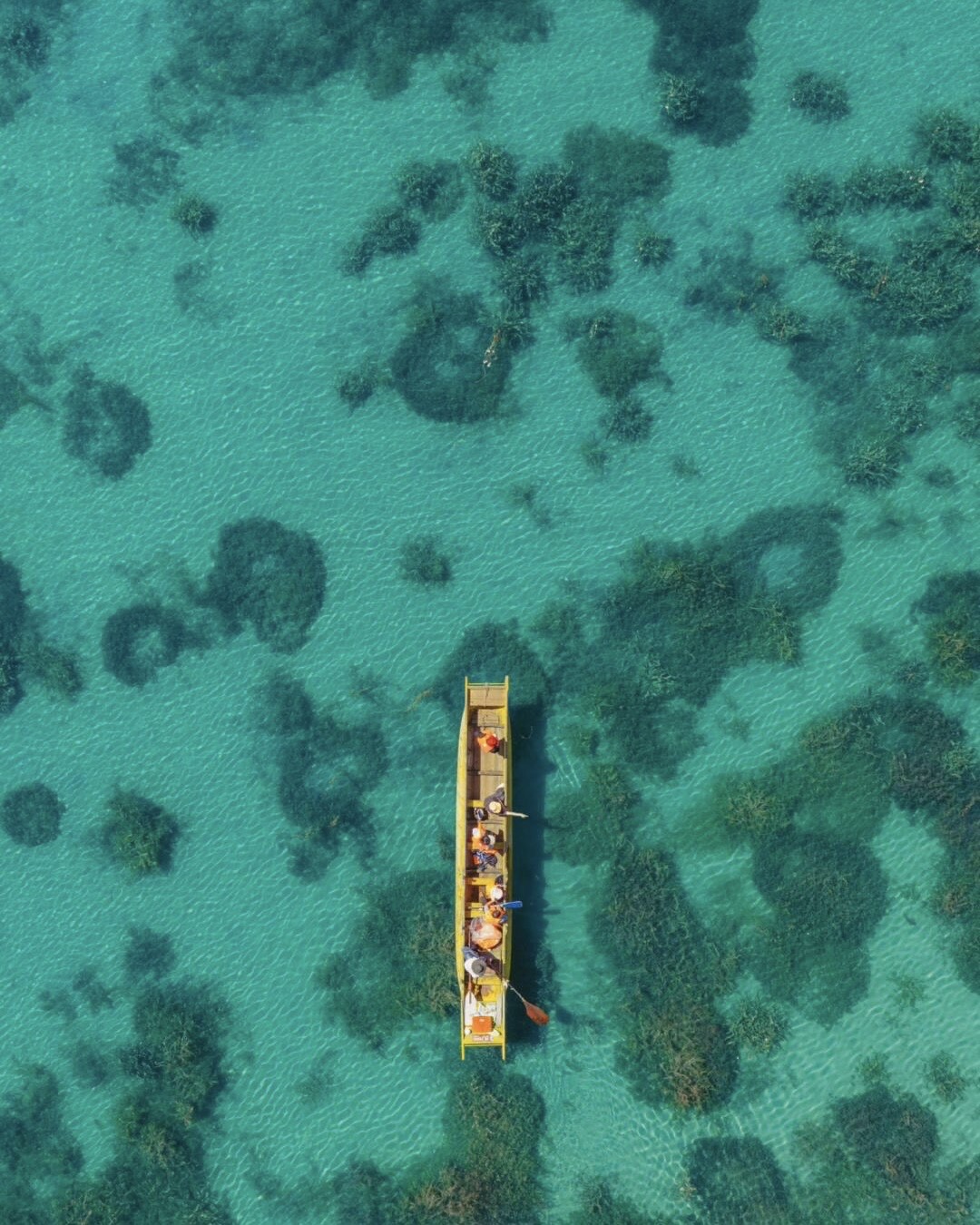 Aerial view of a traditional Mosuo wooden boat carrying passengers over clear turquoise water at Lugu Lake.