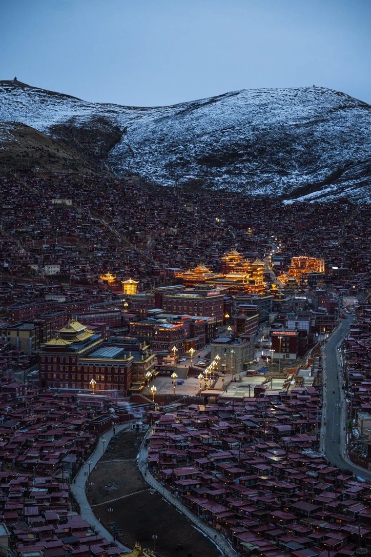 Golden-lit temple halls glowing amid a valley of red houses beneath a snow-dusted mountain at twilight in Seda.