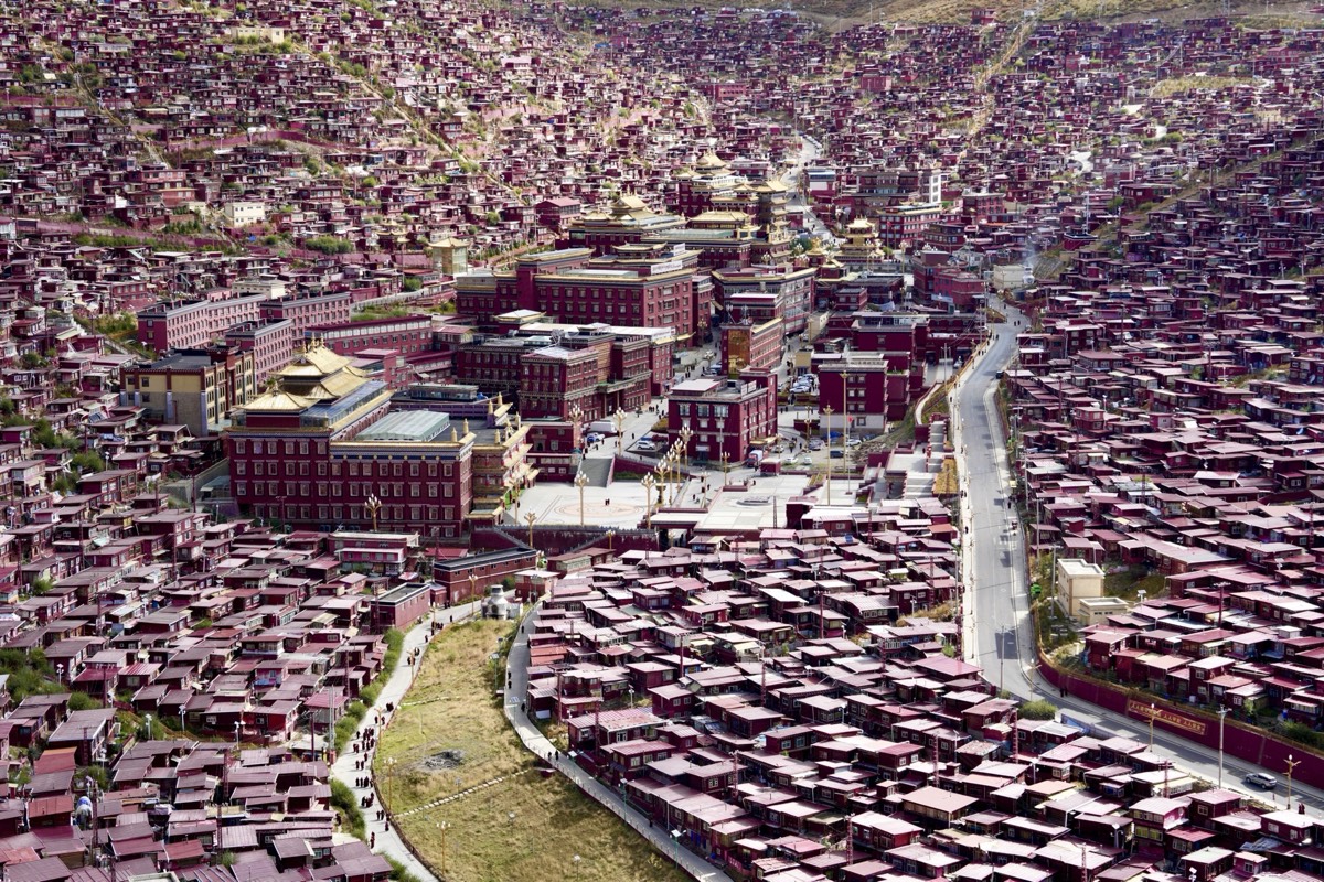 Aerial view of Seda's sprawling settlement of red houses surrounding golden-roofed monastery halls and a central plaza.