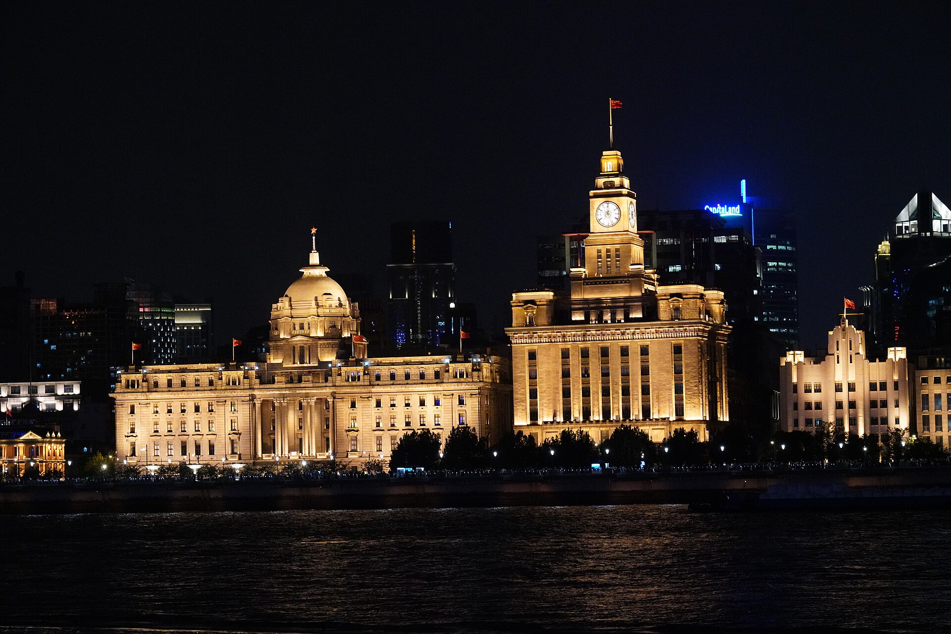 The floodlit colonial banking row of the Bund glowing gold at night — the domed former HSBC building and the Customs House clock tower (海关大楼) — across the Huangpu River, Shanghai